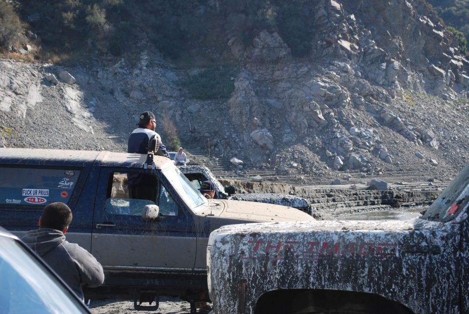 Mud-covered dark blue and tan Ford Bronco with a person sitting on the roof