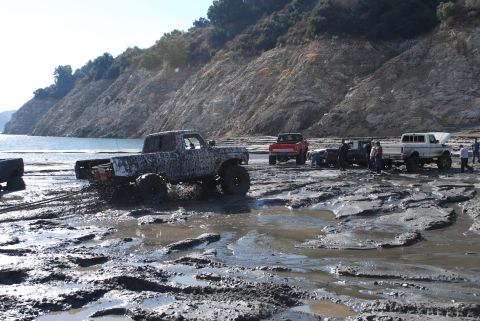 1996 Ford Bronco - Off-roading trucks navigating a muddy terrain next to a lake.