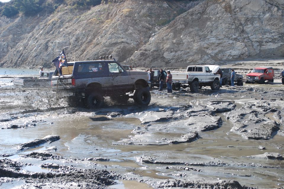 Gray Ford Bronco with lifted suspension splashing mud, seen from the front-left