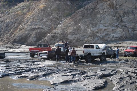 1996 Ford Bronco - Multiple off-road vehicles are bogged down in a muddy, rocky terrain with people observing.