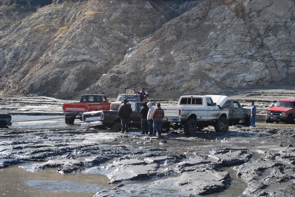 Several trucks and a Bronco stuck in thick mud with people around