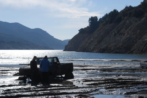 1996 Ford Bronco - Two people stand beside a muddy truck that appears to be stuck in a muddy, watery area with hills in the background.