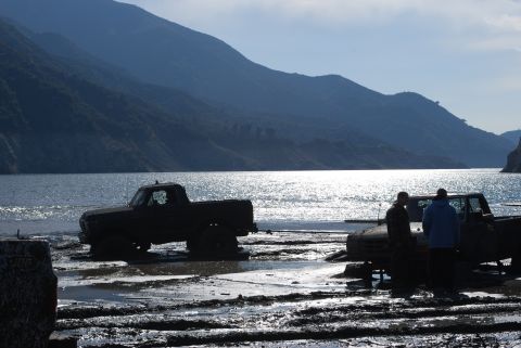1996 Ford Bronco - Two trucks are stuck in the mud by a lake with mountains in the distance.
