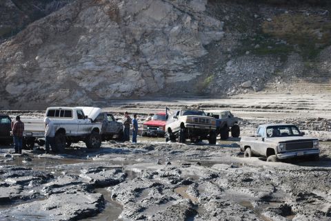 1996 Ford Bronco - Off-road vehicles navigate a challenging muddy terrain with a steep, rocky backdrop.