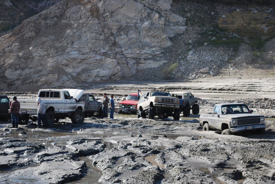 Several lifted trucks stuck in thick mud near a rocky hillside