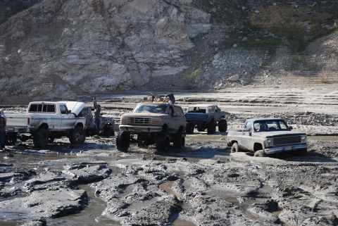 1996 Ford Bronco - Several off-road vehicles navigate a muddy terrain with rocky hills in the background.