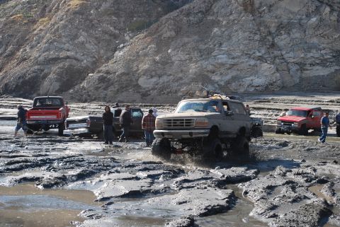 1996 Ford Bronco - Several off-road vehicles, including a 1996 Ford Bronco, are stuck in thick mud.
