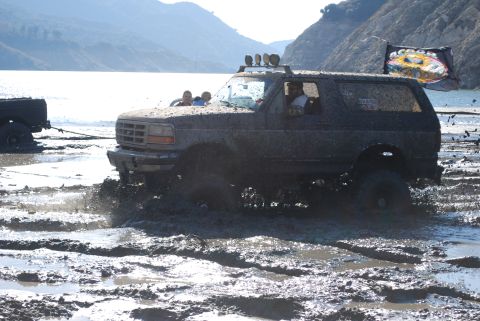 1996 Ford Bronco - Muddy 1996 Ford Bronco navigating a difficult off-road terrain with passengers.