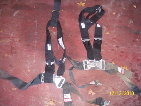 1978 Ford Bronco - Two black racing seatbelts with silver buckles are shown on a red surface, possibly a floor or workbench.