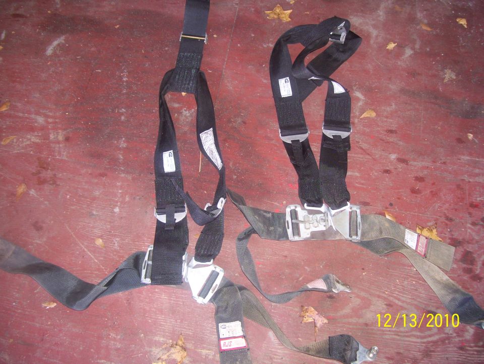 Two black racing seatbelts with silver buckles laid out on a red surface