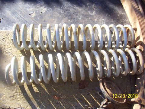 1978 Ford Bronco - Two used suspension coil springs are shown laid out on a rough surface, with a rusty brake rotor nearby.