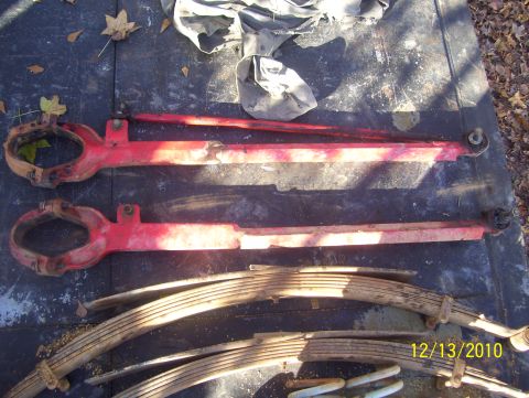 1978 Ford Bronco - Several automotive suspension parts, including leaf springs and red arms, are laid out on a dark surface.