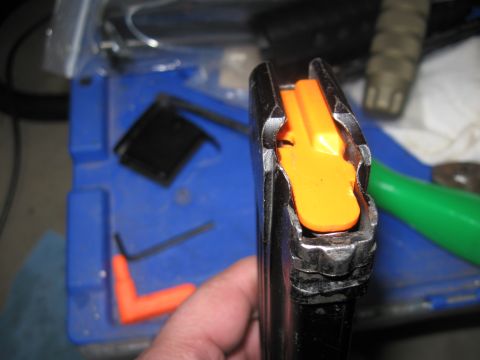 2000 Ford Crown Victoria - A gun magazine with an orange follower is held in a hand, with various tools visible in the background on a blue surface.