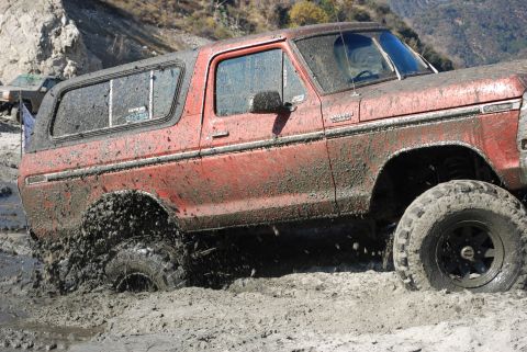 1996 Ford Bronco - This red SUV is deep in the mud, with another vehicle partially visible behind it.