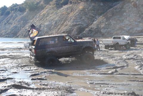 1996 Ford Bronco - A dark blue Ford Bronco navigates through a muddy terrain, with other vehicles and people in the background.