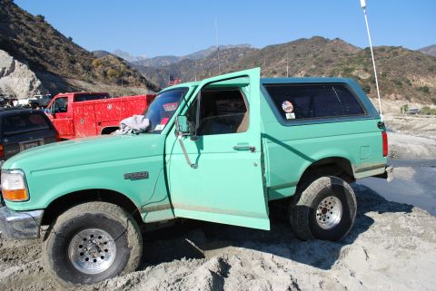 1996 Ford Bronco - Green 1996 Ford Bronco with doors open, parked in a sandy, mountainous area. Another truck is visible.