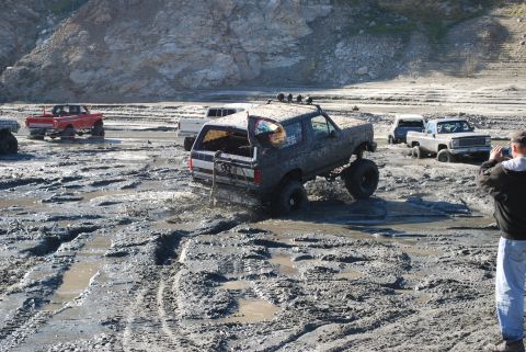 1996 Ford Bronco - Several off-road vehicles navigate a challenging muddy terrain, with one SUV deeply entrenched.
