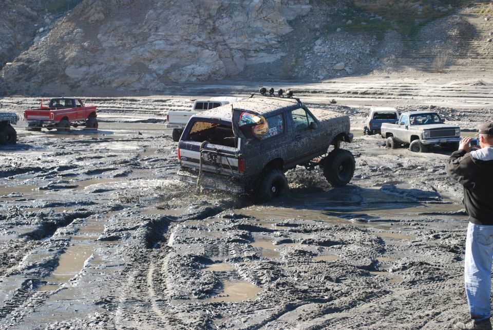 Muddy SUV stuck in mud pit with other trucks around. Person taking photo