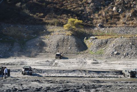 1996 Ford Bronco - Several vehicles navigate a muddy, dry riverbed with steep, terraced banks.