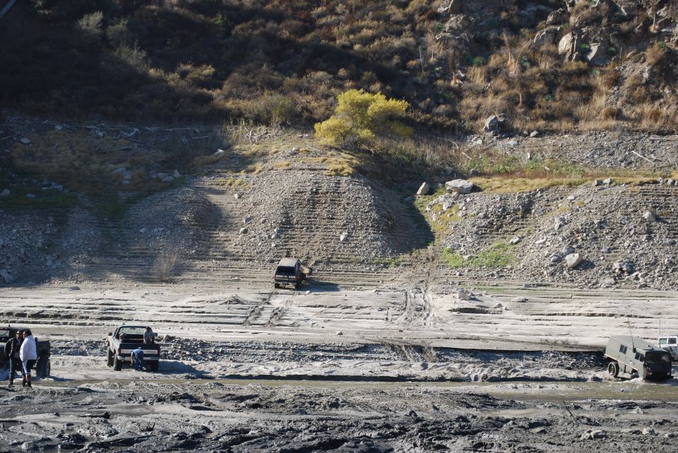Dark SUV driving up muddy embankment with other vehicles nearby