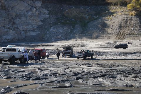 1996 Ford Bronco - A group of off-road vehicles navigate a challenging muddy terrain with a rocky hillside in the background.
