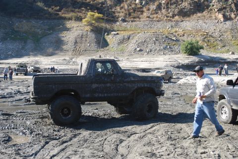 1996 Ford Bronco - A heavily modified Ford Bronco navigates a muddy terrain with other vehicles in the background.