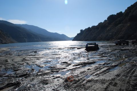1996 Ford Bronco - Trucks navigate a muddy terrain next to a body of water under a clear sky.
