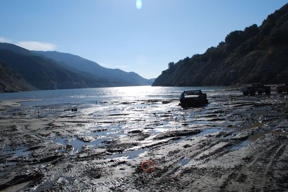 Several trucks stuck in mud near a lake with mountains in the background