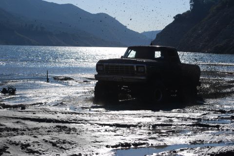 1996 Ford Bronco - Truck stuck in mud near a lake with mountains in the background.