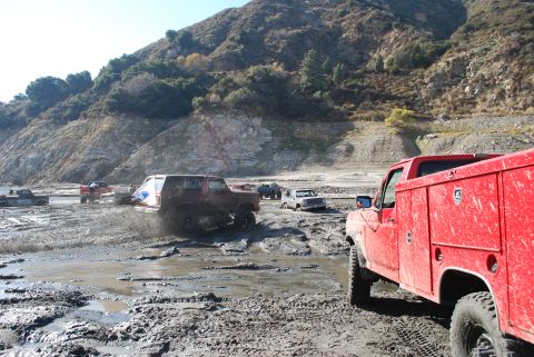 1996 Ford Bronco - Multiple vehicles navigate a challenging muddy terrain with a steep, vegetated hillside in the background.