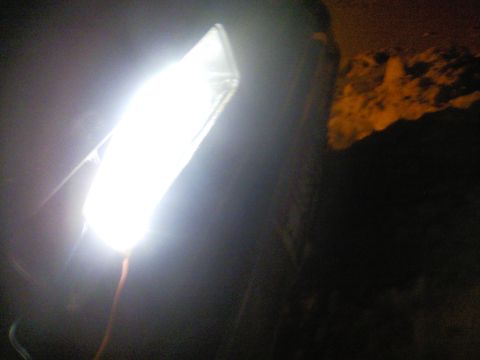 1989 Ford Bronco - A bright headlight illuminates a dark scene, with a portion of a vehicle's body visible.