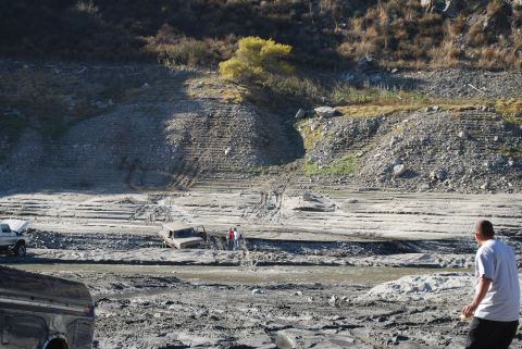1996 Ford Bronco - Multiple vehicles are seen in a muddy, dry riverbed with a steep, rocky embankment in the background.