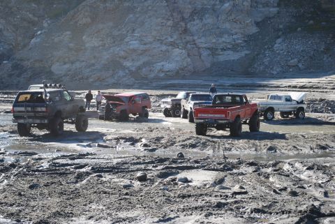 1996 Ford Bronco - Several lifted trucks and SUVs are gathered in a muddy, rocky area, with a "Supermotors" logo visible at the bottom right.