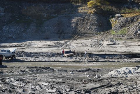 1996 Ford Bronco - Two vehicles are stuck in a muddy, dry riverbed with people observing.