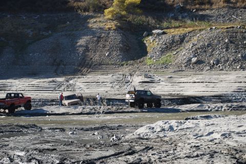 1996 Ford Bronco - Several trucks navigate a challenging, muddy terrain with steep, eroded banks.