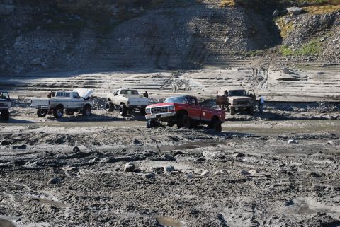 1996 Ford Bronco - Several trucks are gathered in a muddy, dry riverbed with a rocky hillside in the background.