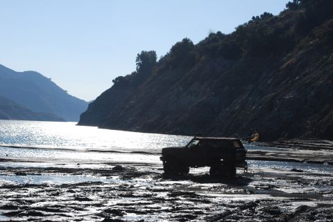 1996 Ford Bronco - A 1996 Ford Bronco sits on a muddy shore near a body of water, with hills in the background.