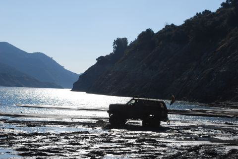 1996 Ford Bronco - 1996 Ford Bronco parked on muddy shore by water with hills in background.