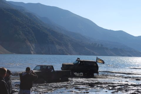 1996 Ford Bronco - Two vehicles are stuck in the mud near a lake, with mountains in the background. One vehicle has a flag attached.