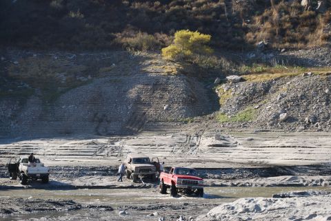 1996 Ford Bronco - Multiple trucks navigate a muddy, dry riverbed under a bright sky.