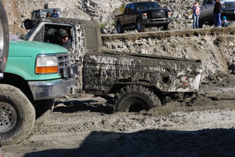 1996 Ford Bronco - Two trucks are stuck in the mud, one green and one heavily covered in mud.
