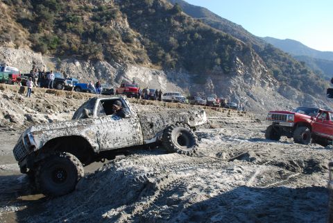 1996 Ford Bronco - Pickup truck navigating a challenging muddy off-road course with spectators watching.