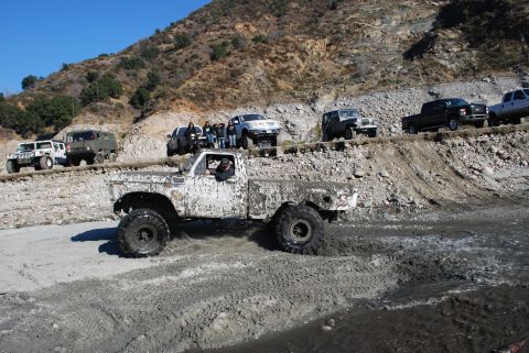 1996 Ford Bronco - Several off-road vehicles navigate a muddy terrain on a sunny day.