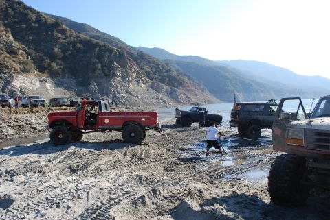 1996 Ford Bronco - Several off-road vehicles are gathered on a sandy bank near a body of water.