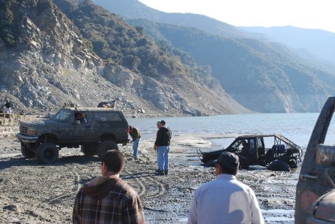 1996 Ford Bronco - Two off-road vehicles are seen by a lake, one is a muddy Ford Bronco, the other is a modified buggy.