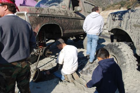 1996 Ford Bronco - People work on a heavily mud-covered off-road vehicle, with another similar vehicle visible nearby.
