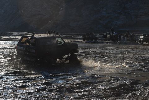 1996 Ford Bronco - A vehicle navigates a muddy terrain, kicking up water as other vehicles and onlookers observe.