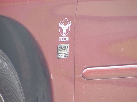 1998 Ford Taurus - Close-up of a red car's fender showing a TCCA 24V DOHC badge and part of the tire.