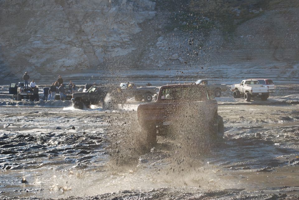 Off-road vehicles splashing mud in a rocky, wet terrain