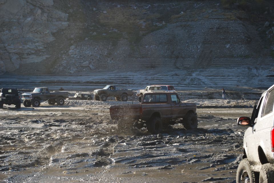 Several modified trucks driving through a muddy off-road course